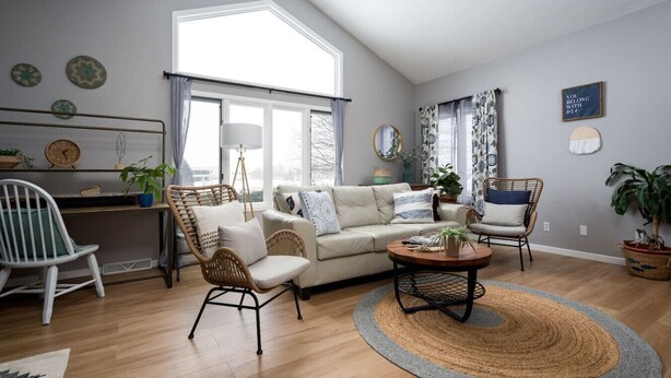 A modern living room with a high ceiling, a sofa, two armchairs, a coffee table, and a desk with a chair.