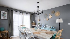 A dining area with a wooden table, white chairs, a chandelier, and decorative wall art.