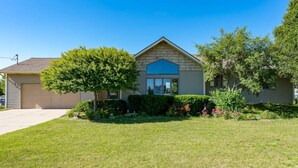 A two-story house with a front garage, a large tree, and a well-maintained lawn.