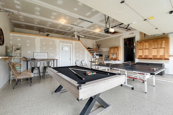Une table de billard, une table de ping-pong et une table de jeu de fléchettes se trouvent dans une pièce dotée d’un plafond en pente et de meubles en bois.