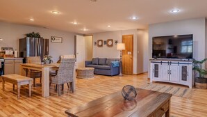 A modern living room with a sofa, dining table, and chairs. There is a kitchen area with a refrigerator and cabinets. A television is mounted on the wall. - Family and big group 14 Guests 11 beds 5 baths (Hudsonville)