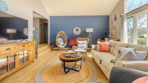 A living room with a sofa, a coffee table, a TV, a wooden cabinet, and a blue wall. - Family and big group 14 Guests 11 beds 5 baths (Hudsonville)