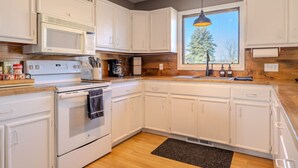 A modern kitchen with white cabinets, a built-in microwave, a stove, and a window providing natural light. - Family and big group 14 Guests 11 beds 5 baths (Hudsonville)