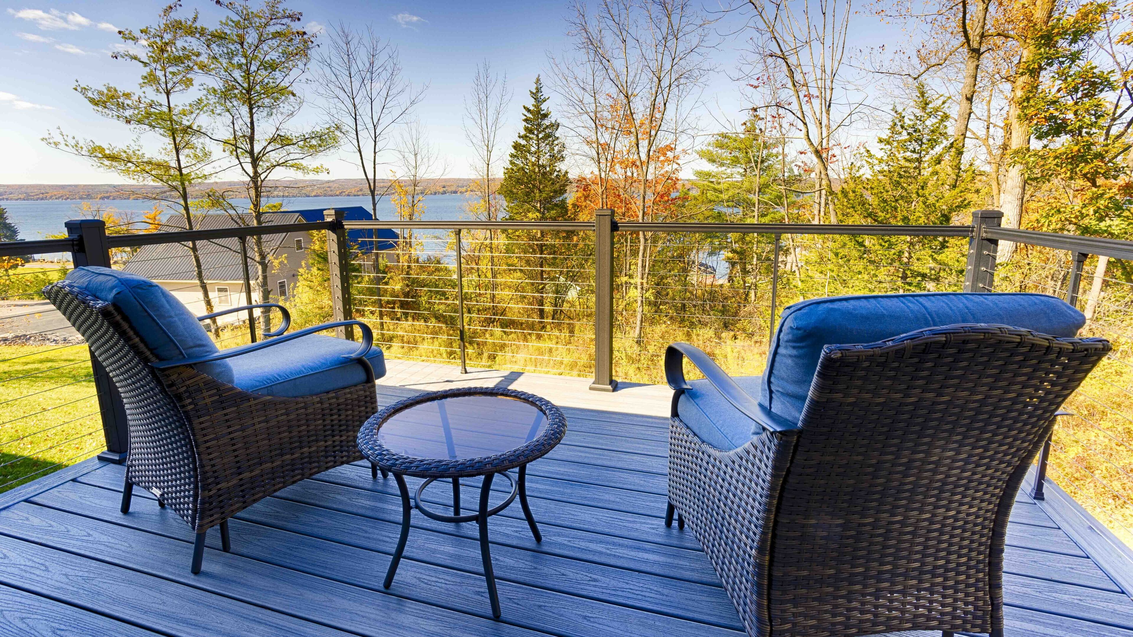 Une terrasse dotée de chaises en osier et d’une petite table, offrant une vue sur une étendue d’eau et des arbres.