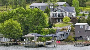 Une propriété située au bord de l’eau, comprenant plusieurs maisons, des bateaux amarrés et un espace abrité avec des chaises.