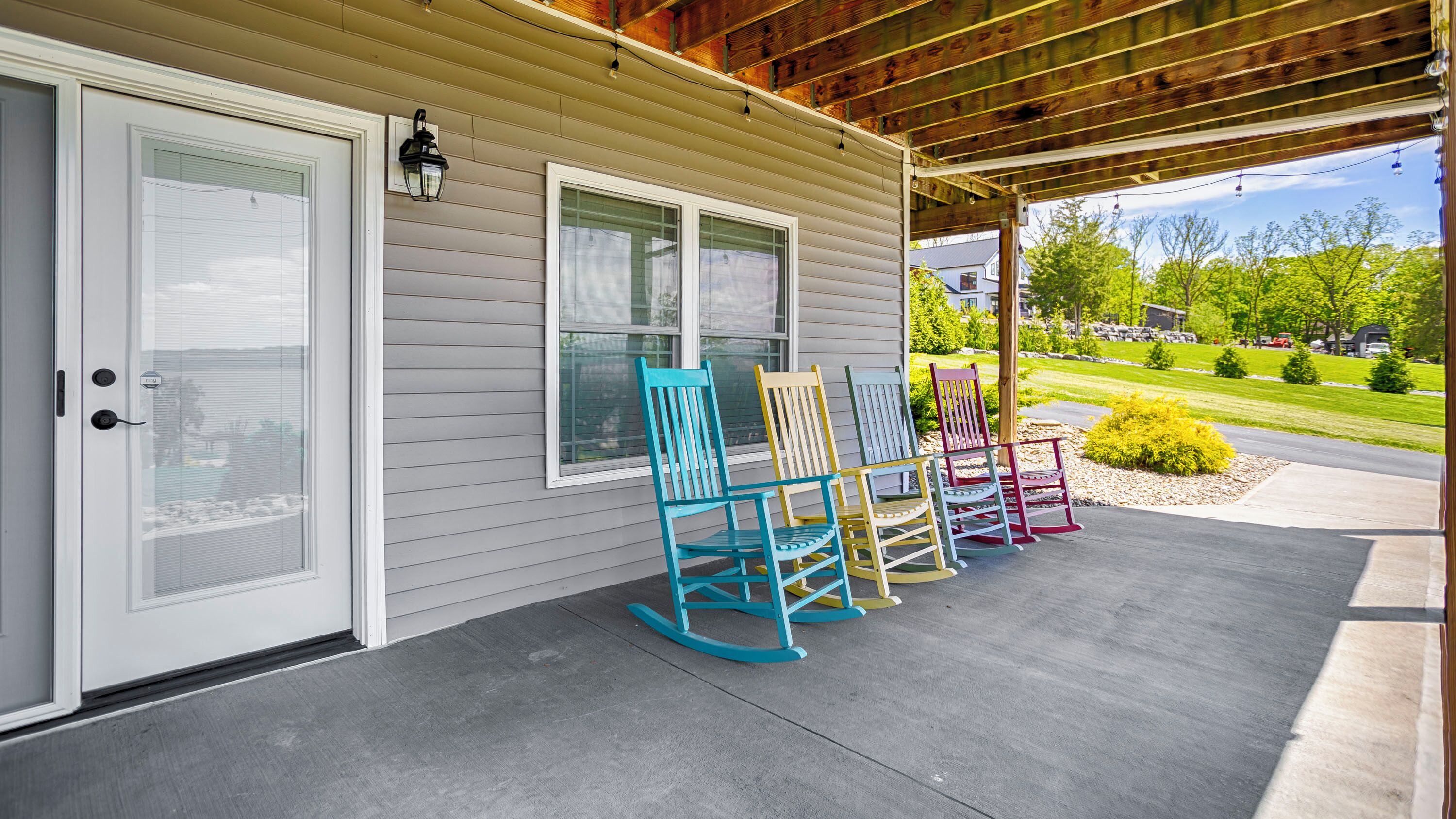A covered porch with a sliding glass door, a wooden ceiling, and a row of colorful rocking chairs.