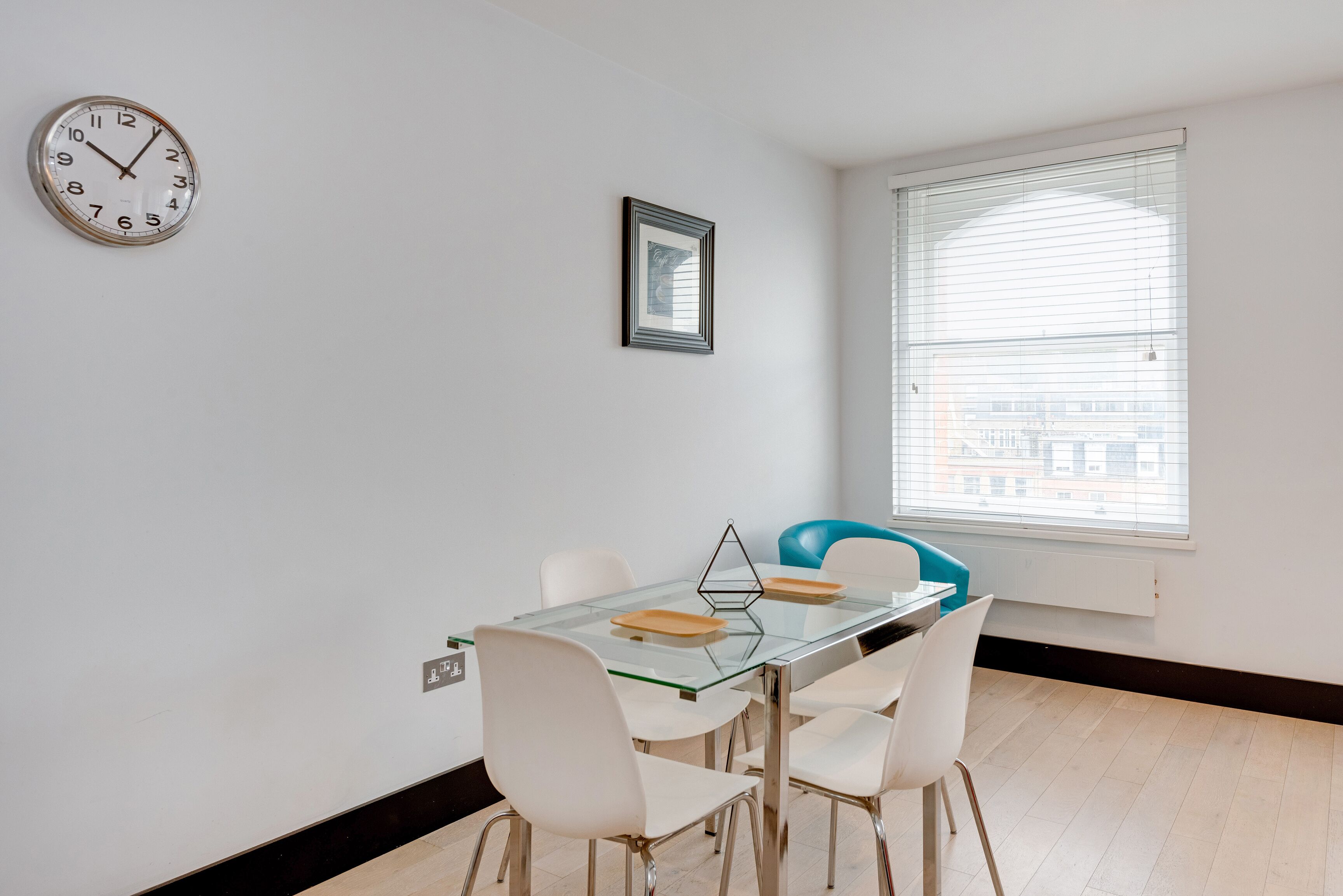 A modern dining area with a glass table, white chairs, and a clock on the wall.