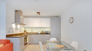 A compact kitchen with a glass dining table, white chairs, and a red sofa. - Heinze Building by City Living London (London)