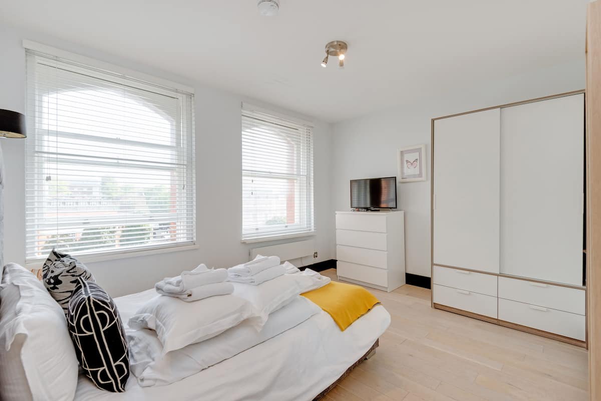 A bedroom with a bed, white walls, a wardrobe, and a television on a dresser.