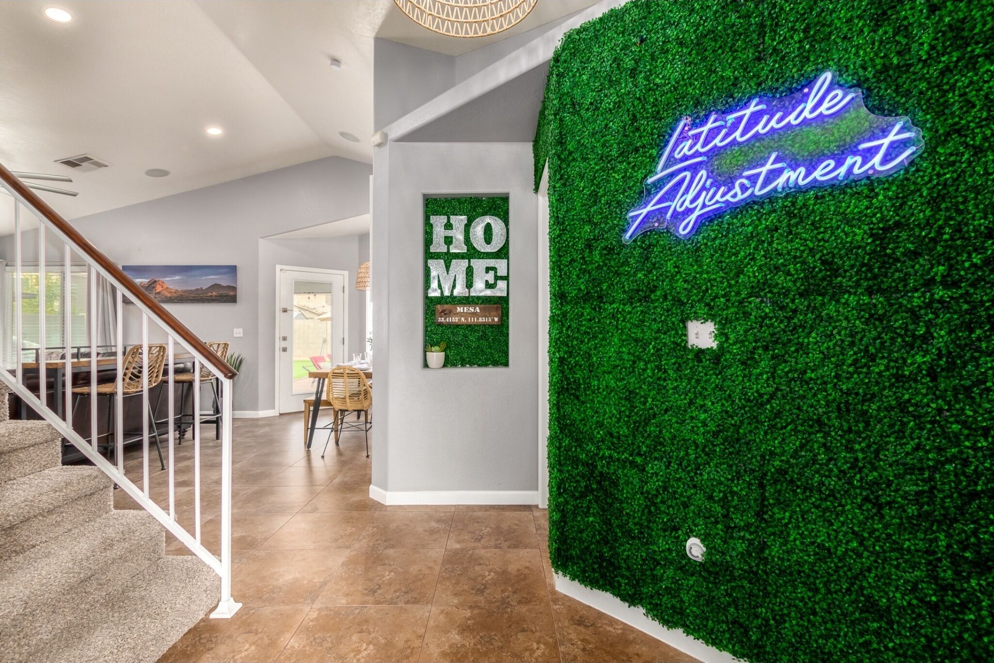 Un interior moderno con una escalera, una pared verde con un letrero de neón, y un cartel que dice 'HOME'.