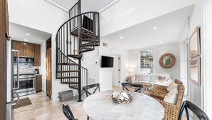 Un amplio salón con una mesa de mármol, muebles de mimbre y una escalera espiral negra.
