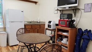 Une cuisine compacte équipée d’un réfrigérateur, d’un four à micro-ondes et d’un four traditionnel. On y trouve une table à manger avec des chaises, ainsi qu’une petite étagère contenant de la vaisselle et un four à micro-ondes.