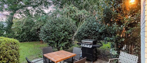 Un patio al aire libre con mesa, sillas, una parrilla y un banco.