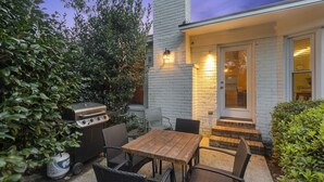 An outdoor patio with a wooden table and chairs, a grill, and a brick wall.
