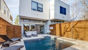 Une maison moderne dotée d’une piscine, d’un espace salon extérieur et d’une clôture en bois.