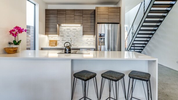 Une cuisine moderne dotée d’un îlot central, de tabourets de bar et d’un escalier.