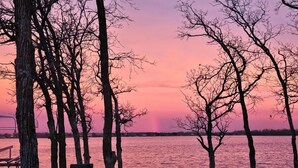 Un parc a la vora d'un llac amb taules de pícnic i bancs, envoltat d'arbres, durant el capvespre.