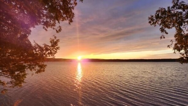 Un coucher de soleil sur un lac paisible, avec une jetée en bois et des chaises.
