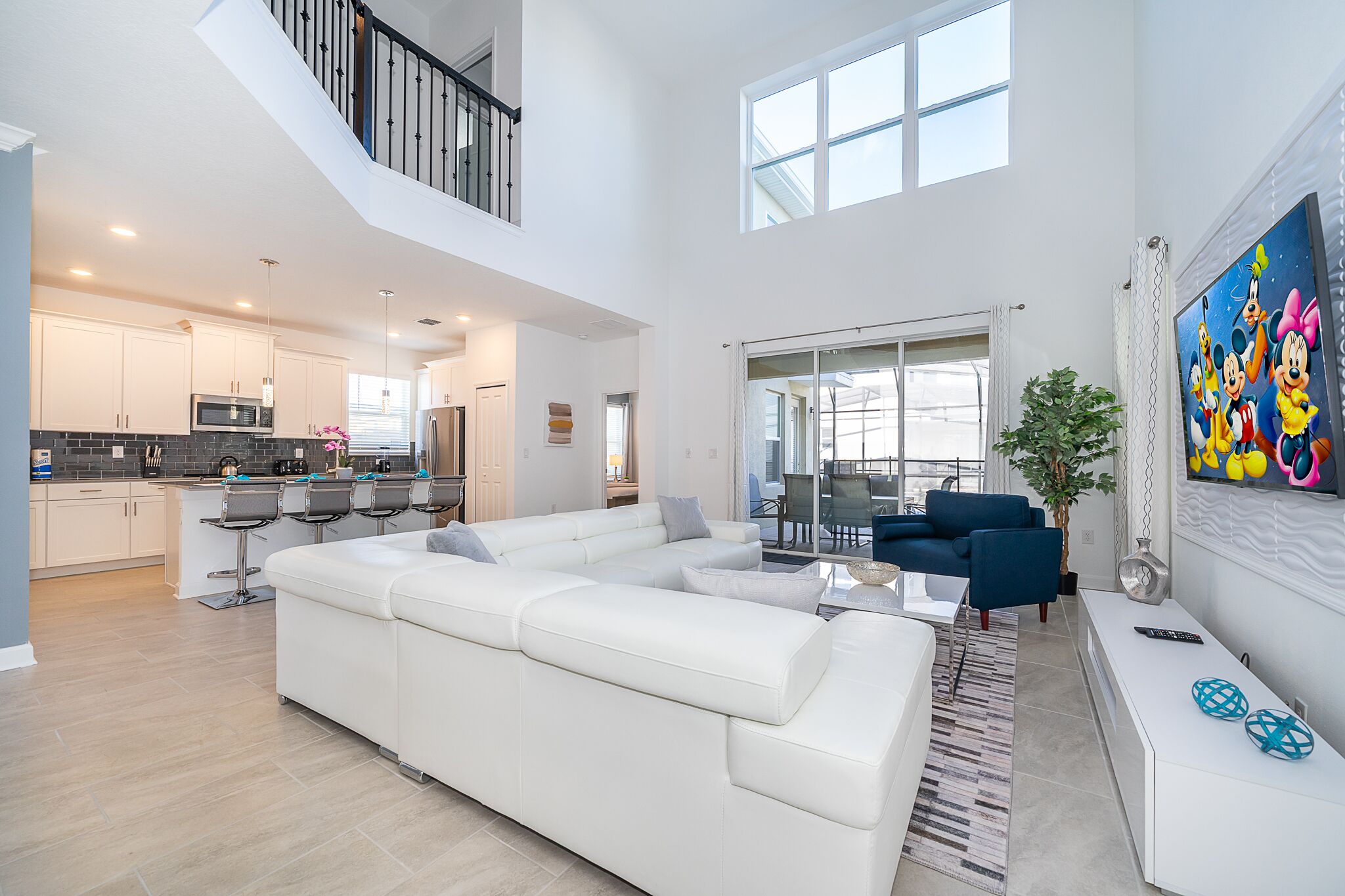 A spacious living area with a white sectional sofa, a dining table with chairs, and a kitchen in the background.
