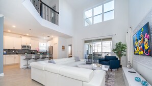Een ruime woonkamer met een witte modulaire bank, een eettafel met stoelen, en een keuken op de achtergrond.