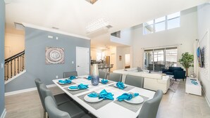 Een moderne eethoek met een lange tafel voor zes personen, een trap en uitzicht op de woonkamer.