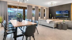 Una sala de estar moderna con comedor, sofás grises, una mesa de madera y un televisor montado en la pared.