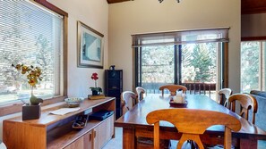 A dining area with a wooden table and chairs, a vase with flowers, and a bookshelf. - Snowcreek I 28, Light and Bright Corner Condo with Mountain Views and Fireplace by RedAwning (Mammoth Lakes)