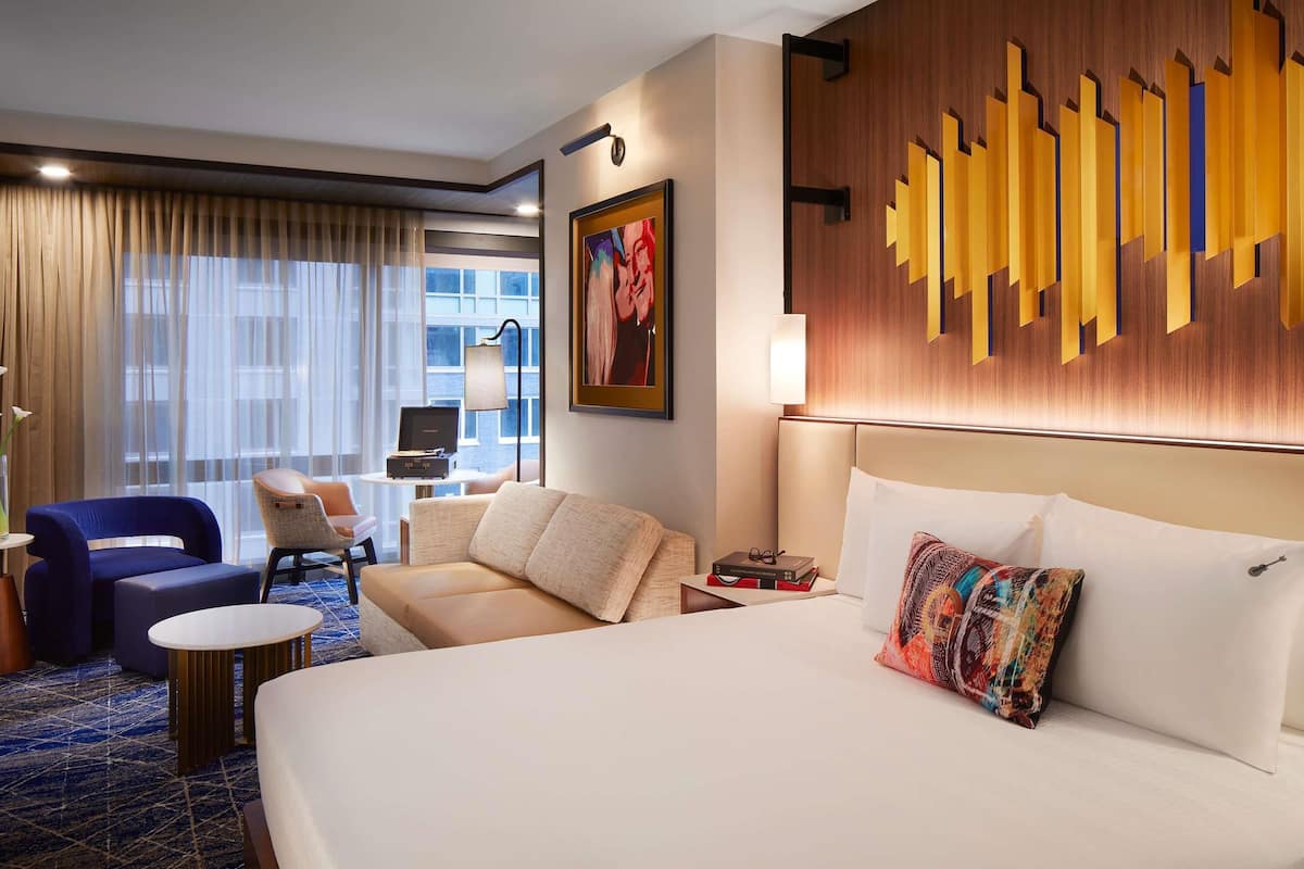 Una habitación de hotel con una cama grande, un sofá, una silla, una mesita y un escritorio con lámpara.