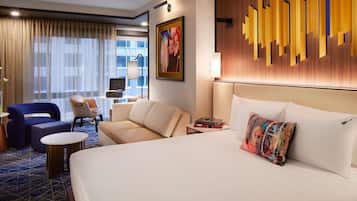 Una habitación de hotel con una cama grande, un sofá, una silla, una mesita y un escritorio con lámpara.