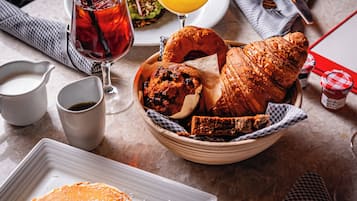 Desayuno con tortitas, cruasanes, magdalenas y un vaso de zumo de naranja sobre una mesa.