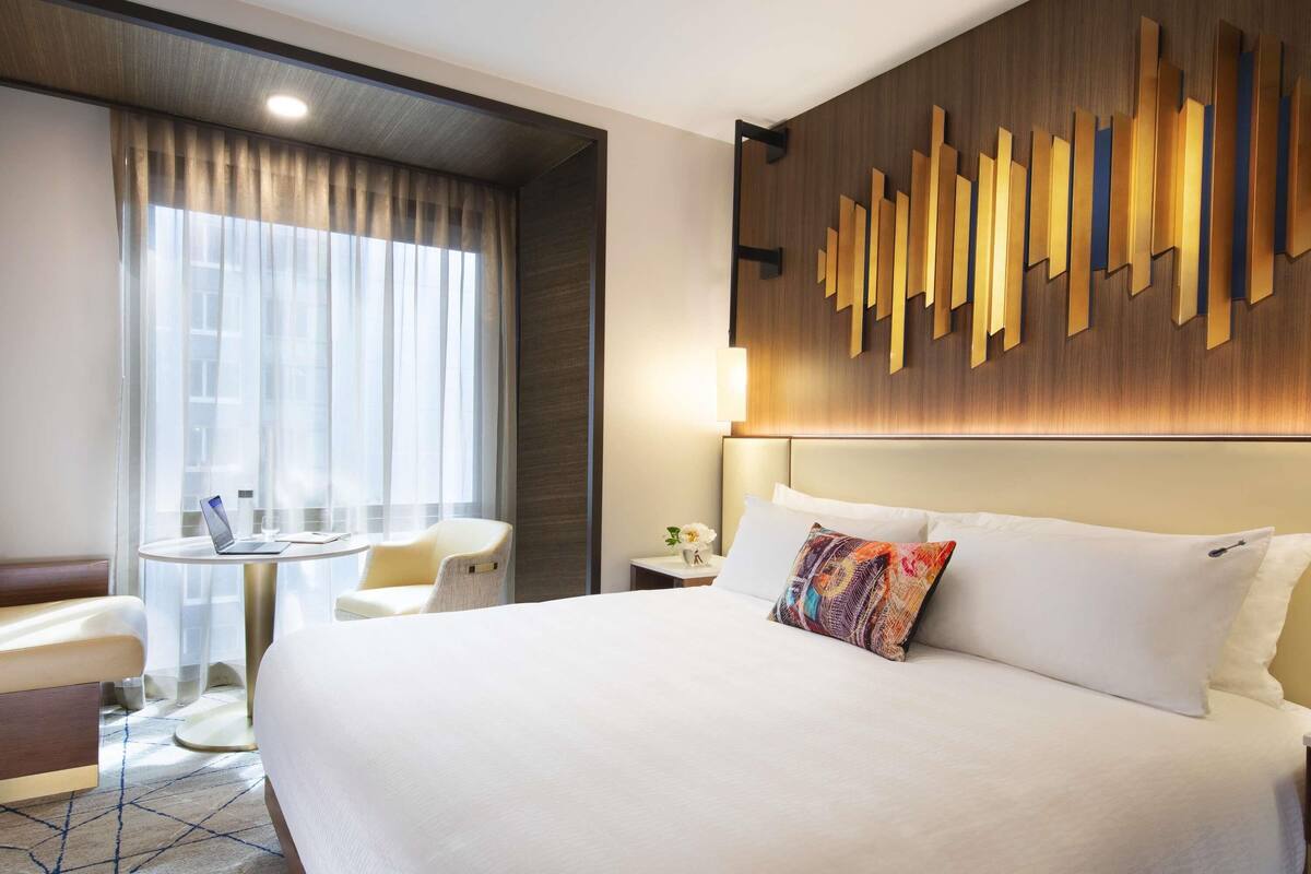 Habitación de hotel con una cama grande, un escritorio con una computadora portátil, una silla y un panel decorativo en la pared.