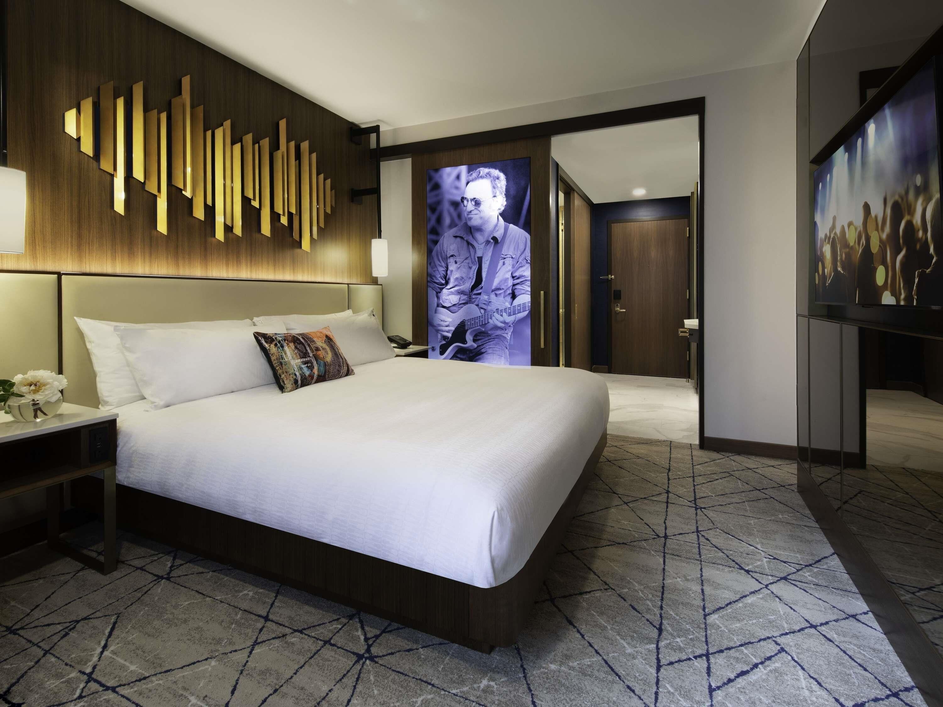 A modern hotel room with a large bed, a wall-mounted TV, and a patterned floor.