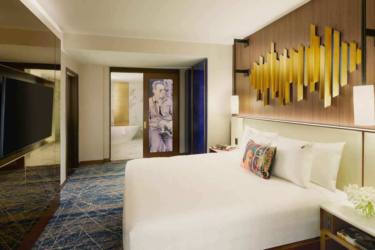 A hotel room with a large bed, a TV, a bathroom with a bathtub, and a decorative wall panel.