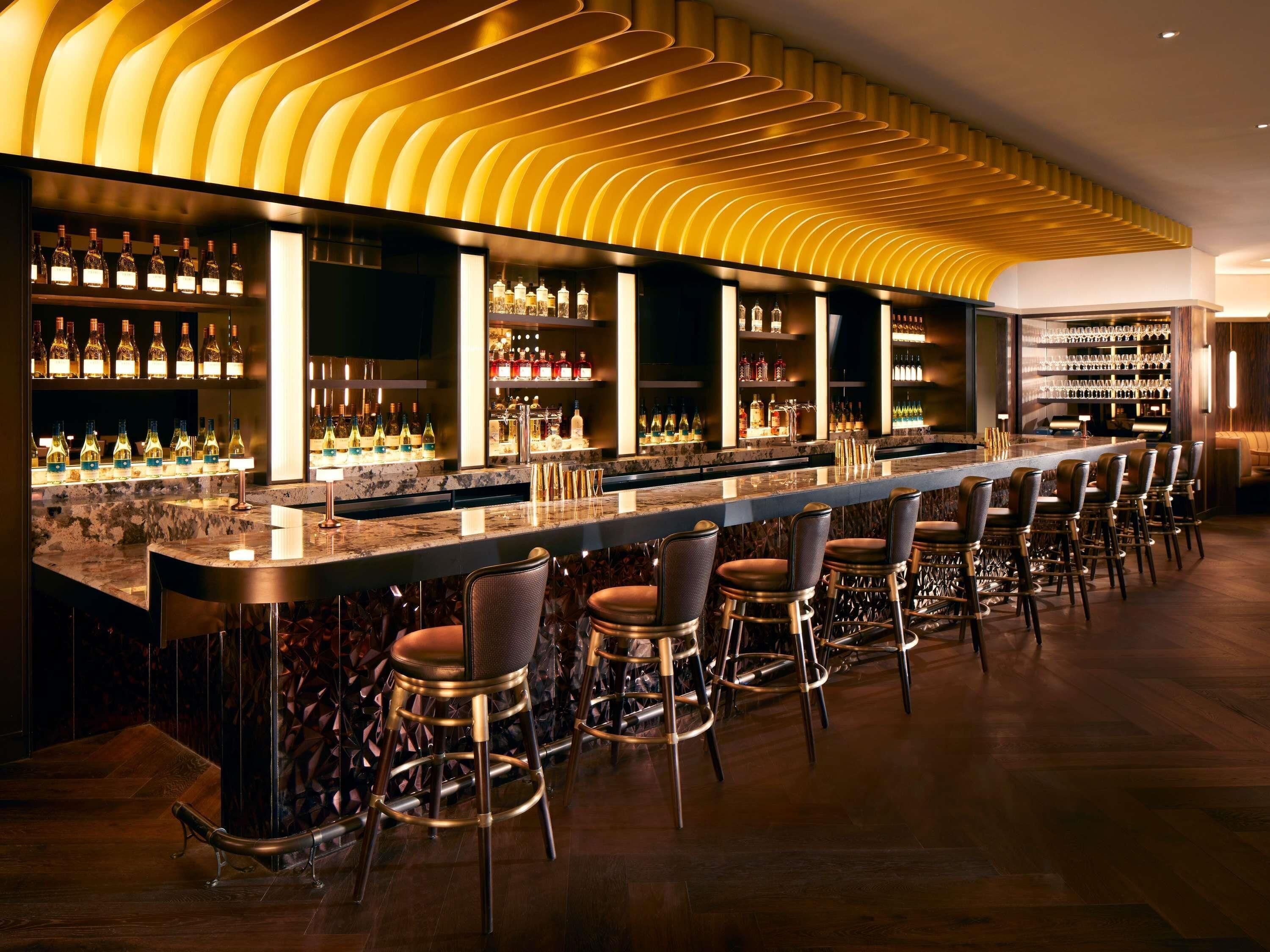 Eine Bar mit einer langen Theke, mehreren Hockern und Regalen voller Flaschen.