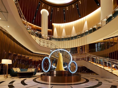 A multi-level interior with a central circular light installation, glass railings, and a staircase.