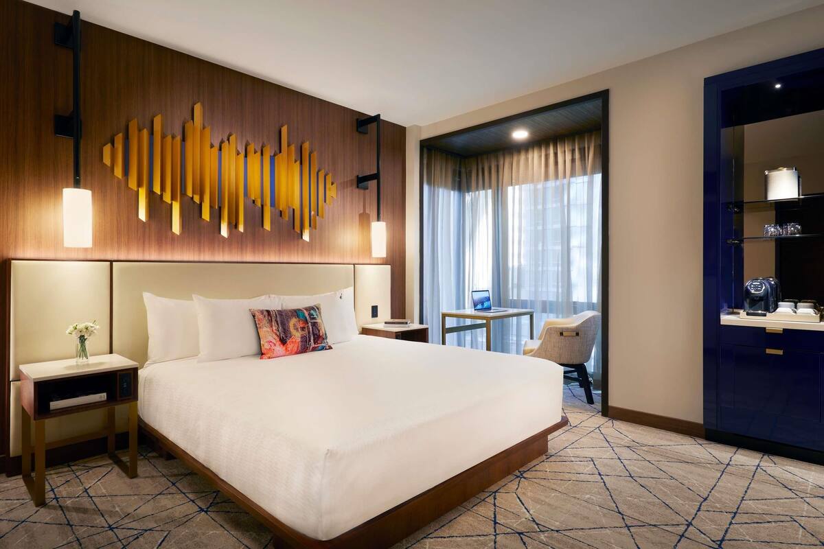 Habitación de hotel con una cama grande, un escritorio con una computadora portátil, una silla y vistas a la ciudad a través de la ventana.