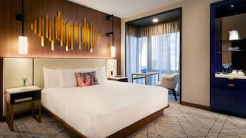 A hotel room with a large bed, a desk with a laptop, a chair, and a view of the city through the window.