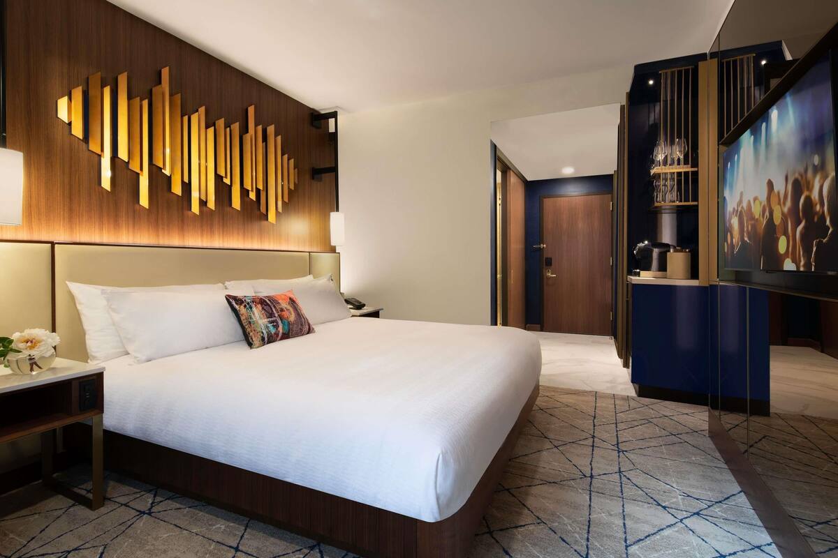 Habitación de hotel con una cama grande, cabecera de madera, una obra de arte en la pared, televisor y minibar.
