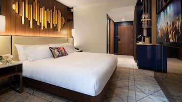 A hotel room with a large bed, a wooden headboard, a wall art installation, a TV, and a minibar.