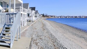 A beachfront property with a wooden deck and a staircase leading to a balcony.