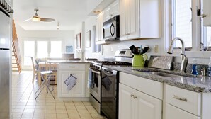 A modern kitchen with white cabinets, a stove, oven, and dishwasher. There is a dining area with a table and chairs.