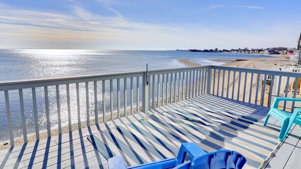 A wooden deck with striped awnings, a sandy beach, and a clear view of the ocean.