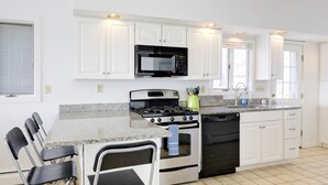 A modern kitchen with white cabinets, a stainless steel stove, a microwave, and a dishwasher. There are four foldable chairs at the counter.