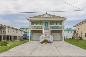 A two-story house with a front porch, a garage, and a small garden. - Beach Break - 4BR Home - 1 Level Living with Covered Porch (Surf City)