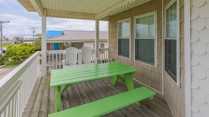 Une véranda couverte avec une table de pique-nique verte et des balustrades blanches.