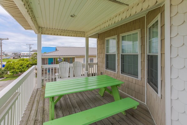 A covered porch with a green picnic table and white railings.