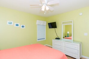 A bedroom with a bed, dresser, ceiling fan, wall-mounted TV, and three framed pictures.