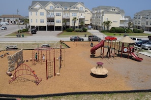 A playground with various play structures, a sandy area, and a parking lot with cars.