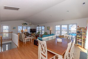 A spacious living room with a wooden dining table, white chairs, a sofa, and a television. - Mermaid Avenue Oceanview 4 Bedroom Home in Surf City – Perfect for the whole (Surf City)
