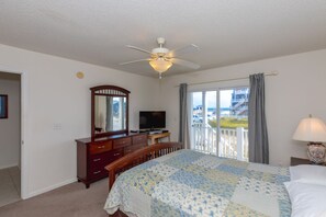 A bedroom with a bed, a dresser, a television, a ceiling fan, a window with a view, and a lamp.